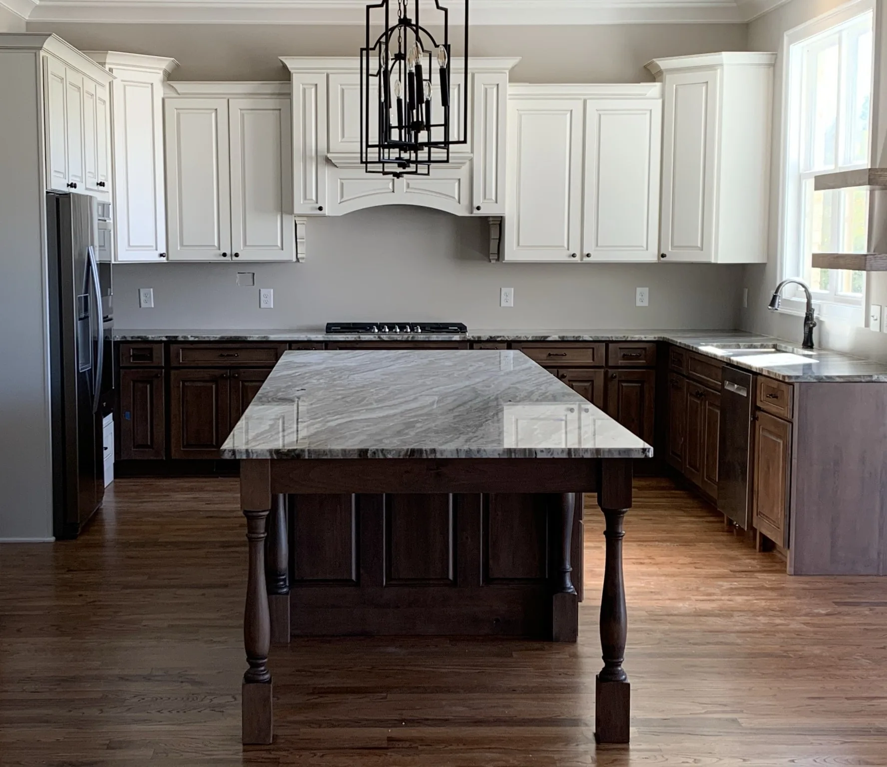 Kitchen with white upper cabinets, dark stained perimeter cabinetry, and a marble island on turned legs