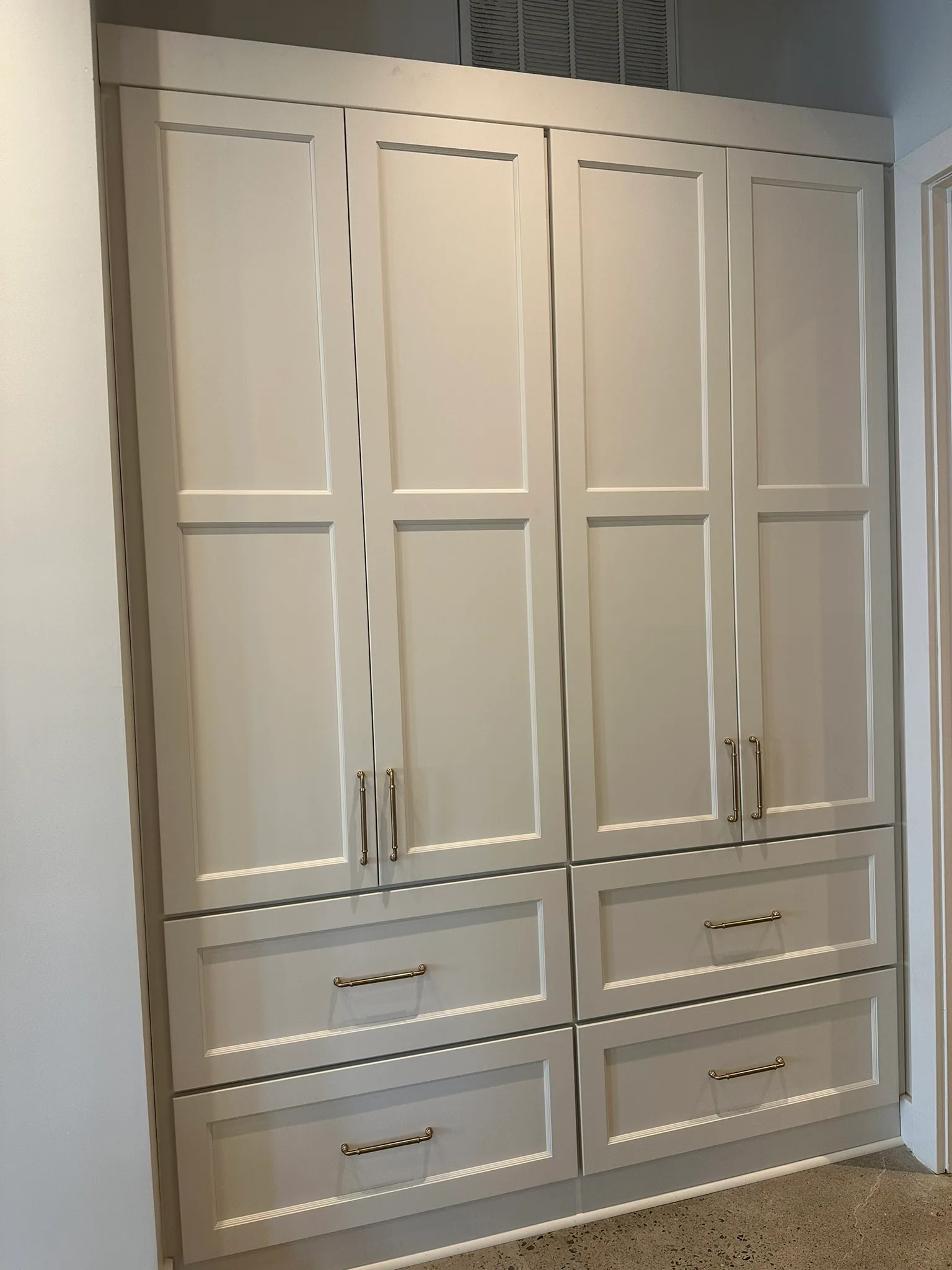 Floor-to-ceiling storage cabinetry with recessed panel doors and brass bar pulls